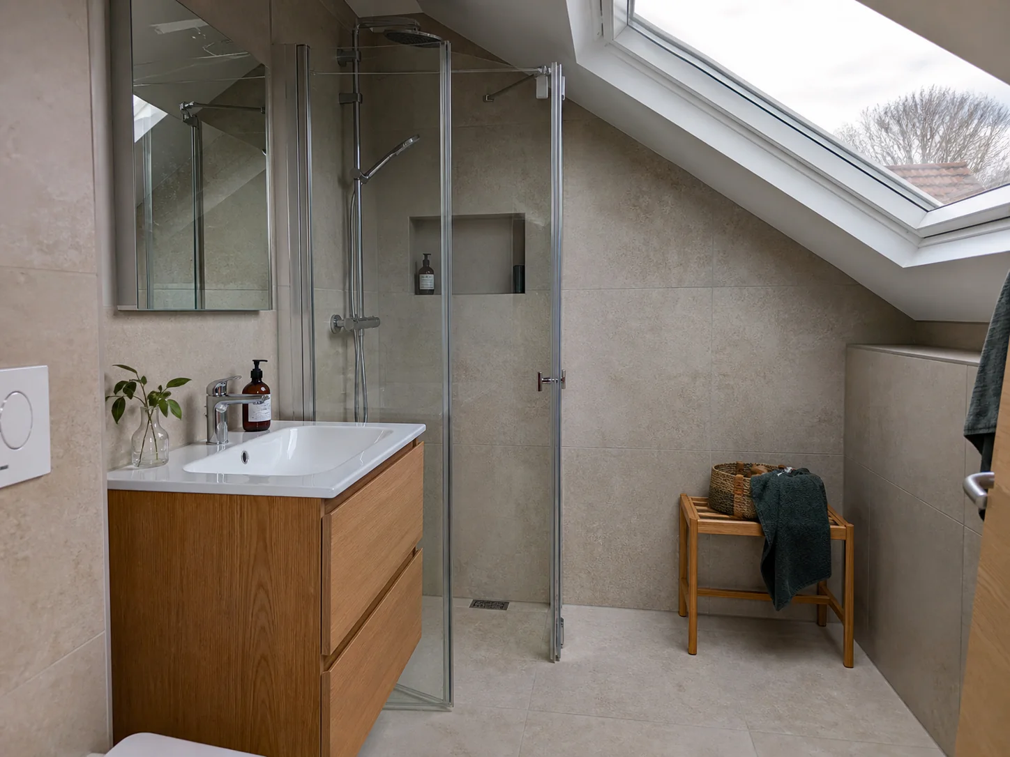 Färdigt vindsbadrum med snedtak, sandfärgade ytor och takfönster